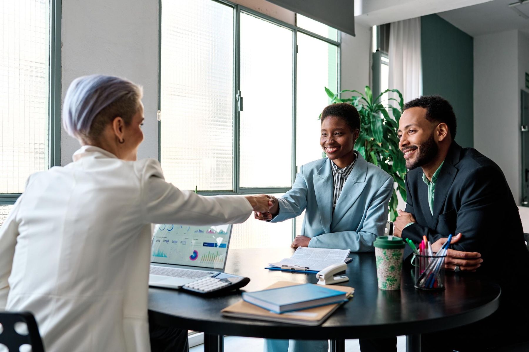 Client and consultants shaking hands across a meeting table